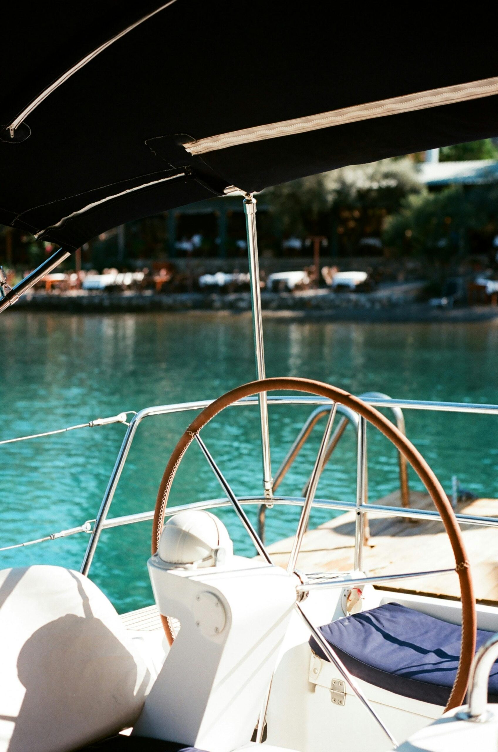 Close-up of a yacht steering wheel overlooking a tranquil bay on a sunny summer day.